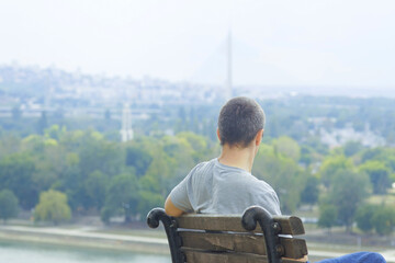 Rear view of man sitting alone on bench and viewing Belgrade waterfront. Concepts of urban escape,...