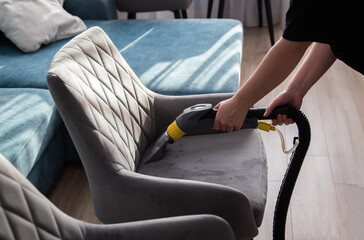 Cleaning a comfortable gray chair with a vacuum cleaner during the day in a modern living room