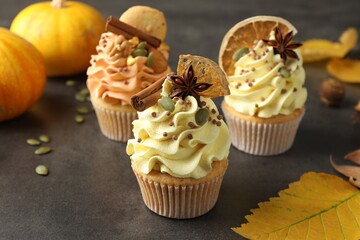 Delicious cupcakes with colorful cream, spices and autumn decor on grey table, closeup