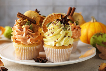 Delicious cupcakes with colorful cream, spices, cookies, nuts and autumn decor on grey table, closeup