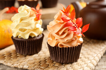Delicious cupcakes with branches with red leaves on wooden table, closeup. Autumn atmosphere