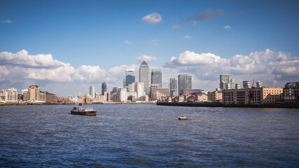 Fototapeta premium Docklands Skyline, London. A panoramic view of the Docklands business district surrounding Canary Wharf with its iconic modern skyscrapers rising above the River Thames under a partly cloudy blue sky.