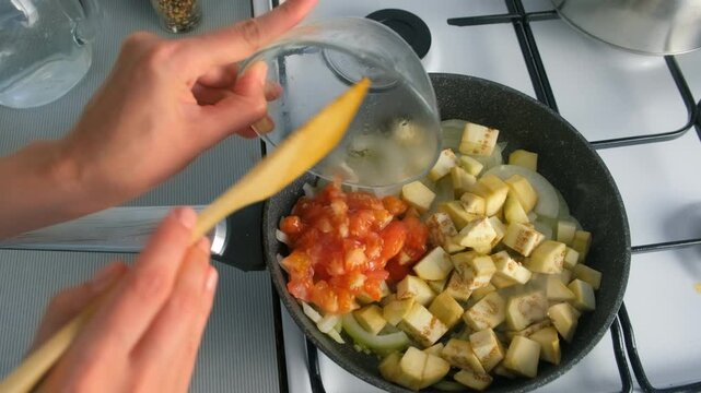 Chef woman hands cooking stirring onions adding eggplant tomatoes to frying pan on gas stove on kitchen. Culinary techniques homemade preparing healthy meal, cook food dish, cuisine, seasoning garlic.