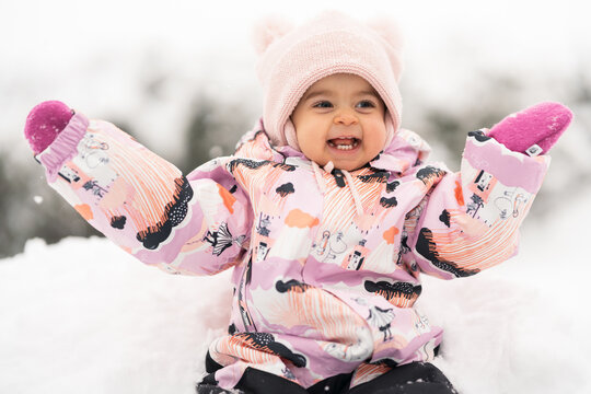 Adorable toddler girl between one and two years old exploring fresh snow outdoors, smiling and joyful in a warm snowsuit and winter hat, symbolizing childhood wonder, winter fun.