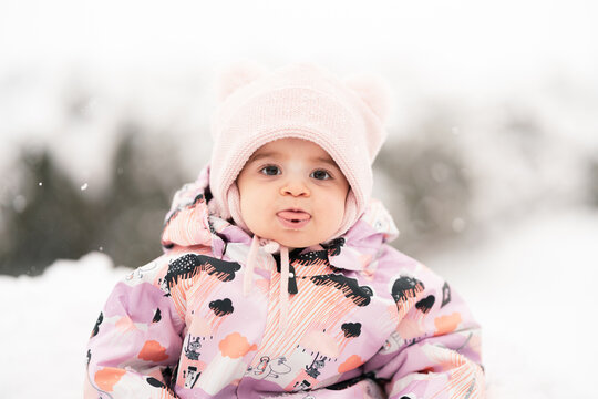 Adorable toddler girl between one and two years old exploring fresh snow outdoors, smiling and joyful in a warm snowsuit and winter hat, symbolizing childhood wonder.