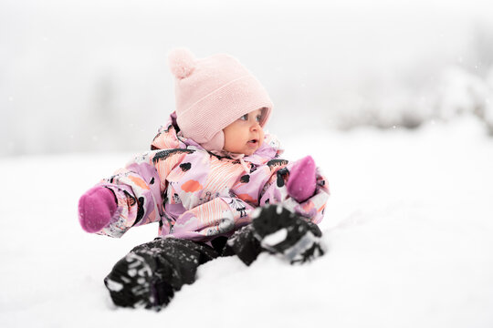 Adorable toddler girl between one and two years old exploring fresh snow outdoors, smiling and joyful in a warm snowsuit and winter hat.