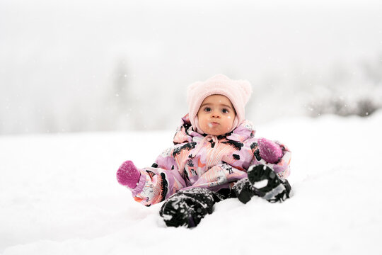 Adorable toddler girl between one and two years old exploring fresh snow outdoors, smiling and joyful in a warm snowsuit and winter hat, symbolizing childhood wonder.