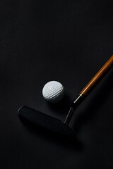 Golf ball and putter with wooden shaft on dark textured surface. Concept of traditional sports gear, luxury branding visuals, performance equipment and classic golf lifestyle.