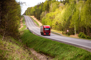Red truck with tarpaulin semitrailer transports cargo on country road. Concept of forwarding driver, cargo transportation and business, industry