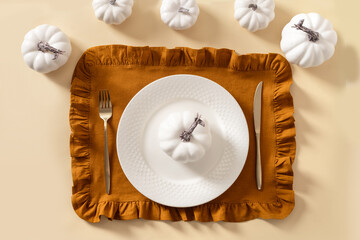 Autumn and Thanksgiving day table setting with plate decorated white pumpkins on beige table. Top view.