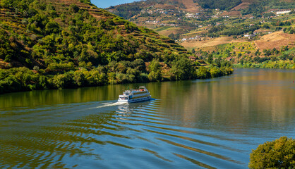 Panorama of the Douro Valley in northern Portugal photographed from the train on a summer day. Picturesque scenery with excursion vessel. Portugal's most beautiful railway line along the riverbank.