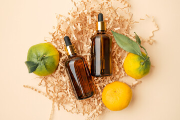 Brown glass cosmetic containers with pipette, fresh tangerines with green leaves, cut craft paper on beige background. Natural cosmetics with vitamin C, organic aroma oil, citrus extract flat lay