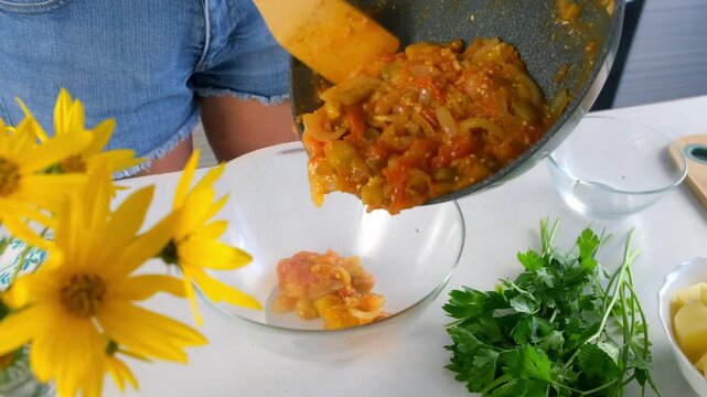 Woman pouring cooked eggplant tomato vegetables stew into glass bowl on kitchen. Culinary techniques, homemade preparing healthy meal cook food dish, cuisine, seasoning garlic.