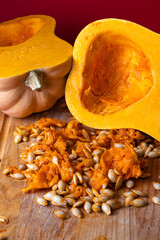 Detailed closeup of raw butternut squash seeds and orange pulp on a wooden cutting board, with cut squash halves in the background. Natural autumn vegetable concept highlighting seasonal harvest
