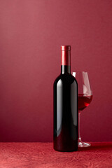 Bottle and glass of red wine on a red background.