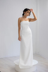 Fashion model in long strapless white dress posing gracefully in studio