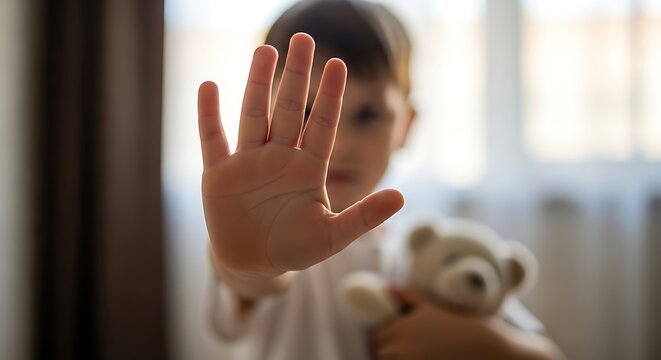 Young child holds teddy bear and raises hand in stop gesture conveying a message of protection and safety against harm