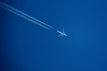 Airplane in the blue sky with contrail, closeup of photo. Airplane in the blue sky with white trace of a plane.