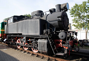 Old steam locomotive on display at a railway museum during a sunny afternoon in a bustling city