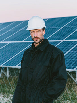 A male engineer wearing a helmet stands at a solar power plant. Installation and maintenance of solar power plants.