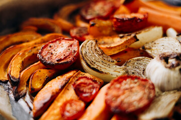 Roasted autumn vegetables pumpkin tomato onion garlic on baking tray, close up.