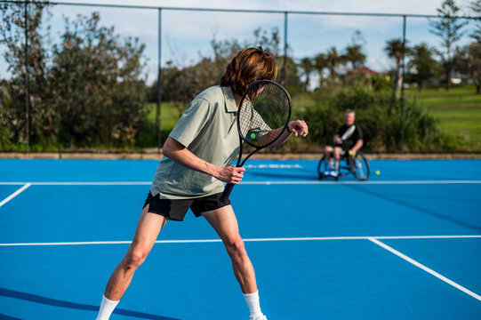 A man on a wheelchair prepares to hit a tennis ball while another player gives him instructions