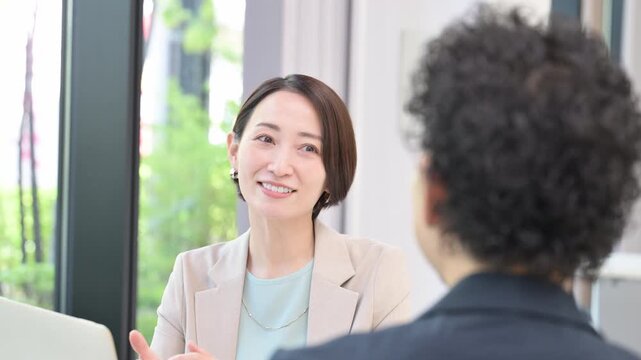 お客様や同僚とデスクに座りパソコンで説明や打ち合わせをする営業女性などの爽やかなイメージ　説明やプレゼンの動画
