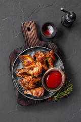 Grilled spicy chicken wings with ketchup in a plate on a dark slate, stone or concrete background. Top view