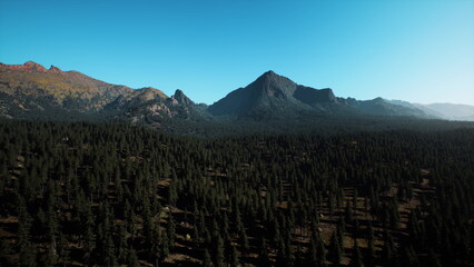 Fototapeta premium Majestic mountains rise over dense green forests, basking under a bright blue sky. Tranquility reigns as nature thrives, creating a perfect backdrop for outdoor adventures.