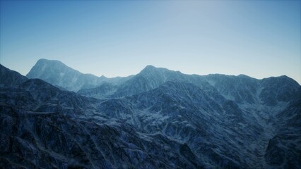 Rugged mountains stretch across the horizon, bathed in soft light as dawn breaks. The landscape is tranquil, with hints of snow accentuating the peaks. Calmness fills the air.