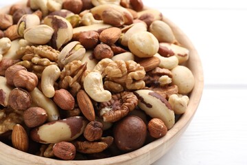 Mix of different nuts in bowl on white wooden table, closeup