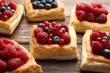 Tasty puff pastries with berries on wooden table, closeup