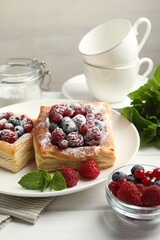 Tasty puff pastries with berries, powdered sugar and mint on white wooden table, closeup