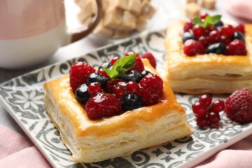 Tasty puff pastries with berries, mint and brown sugar on table, closeup
