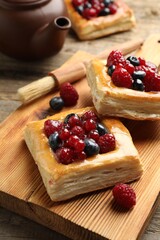 Tasty puff pastries with berries, teapot and brush on wooden table, closeup