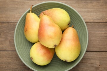 Fresh ripe pears in bowl on wooden table, top view