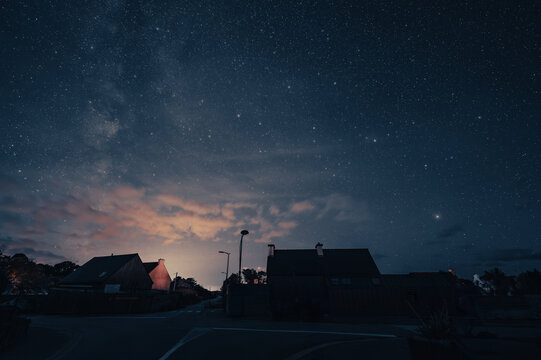 A few house silhouettes against a night sky with many stars.Mysterious atmosphere. A few small clouds are slightly tinged with red by the light from the town.