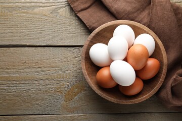 Fresh chicken eggs in bowl on wooden table, top view. Space for text
