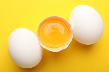 Whole and broken chicken eggs on yellow background, above view