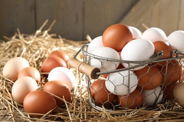 Raw chicken eggs in metal basket and straw on table, closeup