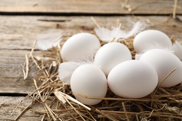 Raw chicken eggs, feathers and straw on wooden table, closeup
