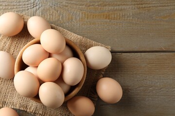 Raw chicken eggs in bowl on wooden table, flat lay. Space for text