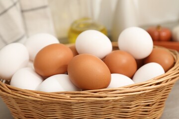 Raw chicken eggs in wicker basket on wooden counter indoors, closeup