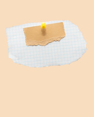 Torn piece of school notebook in a grid and brown piece of paper with beige tape and a pin on beige background