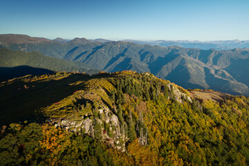 Fototapeta premium Golden sunlight highlights autumn foliage on a highland ridge, with distant mountain peaks fading into soft blue haze, Georgia.