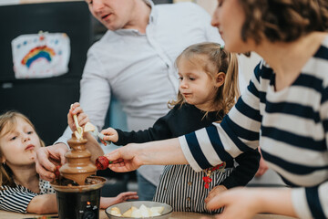 A family gathers around a chocolate fondue, sharing joyful moments and delicious treats.