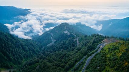 Aerial perspective of a serpentine pass through lush green peaks, with mist filling the valleys below, Georgia