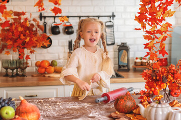 Cute little girl using a red rolling pin to flatten dough for autumn cookies in a rustic kitchen, surrounded by fall decorations like pumpkins and bright maple leaves