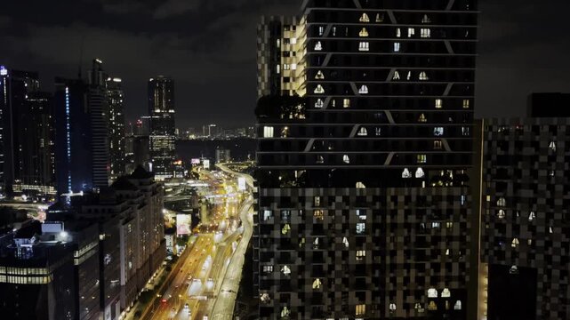A nighttime view of Kuala Lumpur featuring a modern residential tower with illuminated windows, surrounding skyscrapers, and brightly lit highways that highlight the vibrant cityscape of Malaysia