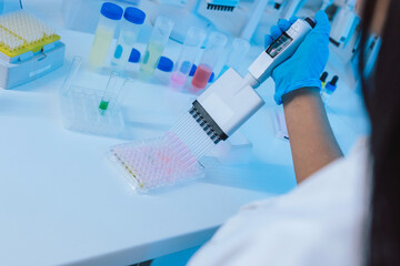 Female lab researcher using a multichannel pipette to fill microplate during the medical clinical analysis.